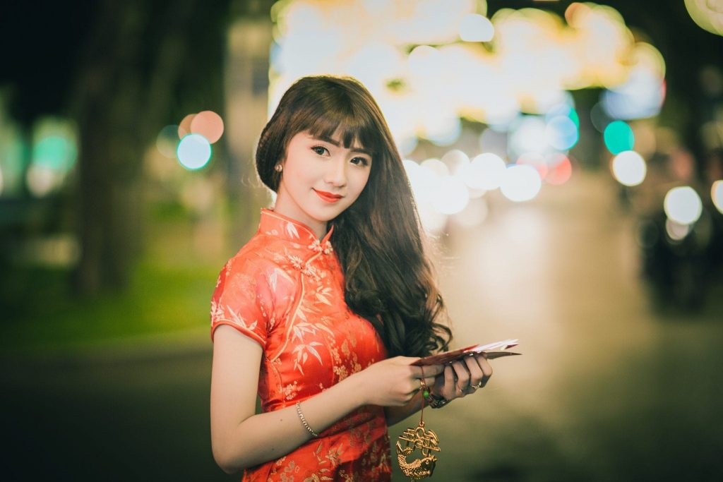 Asian cute girl with long hair who wears a red Cheongsam dress in Chinese  new year theme while she shows her hand to present something on a red  background 19578092 Stock Photo